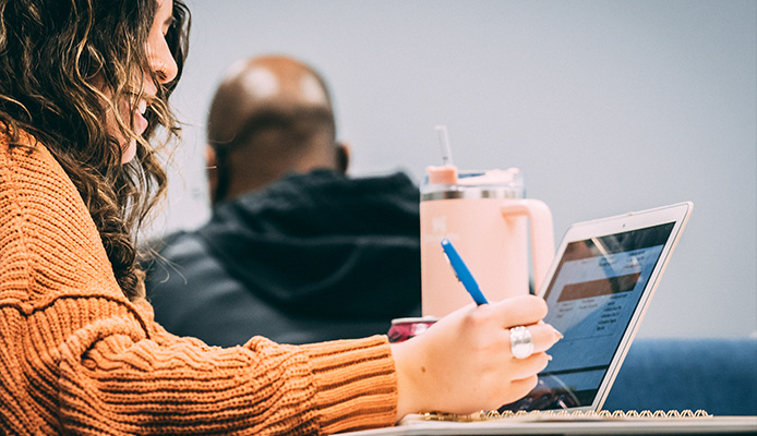 Student smiling and taking notes with computer